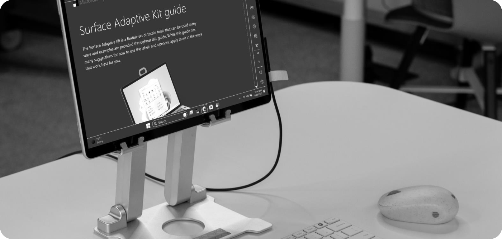 Tablet on a stand showing the Surface Adaptive Kit guide, with a keyboard and mouse on the desk.