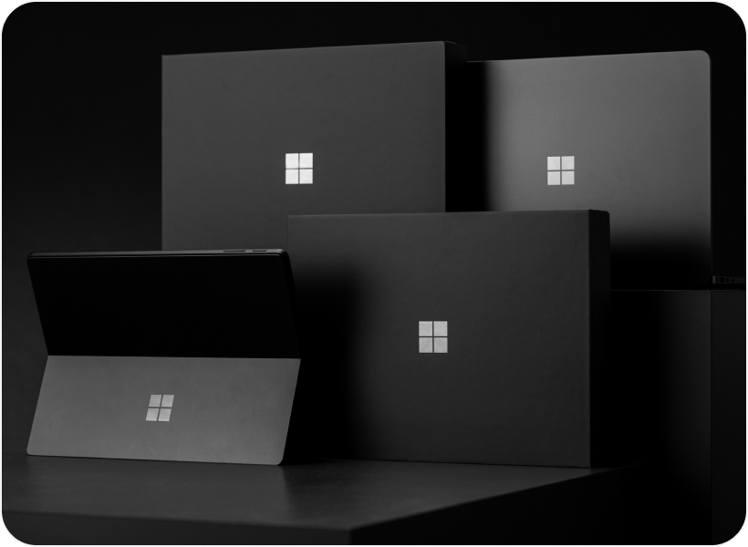 A black Surface Pro and black Surface laptop with black packaging photographed against a black background.
