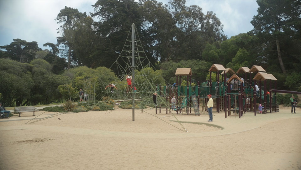 A playground with children climbing on it and an adult nearby.