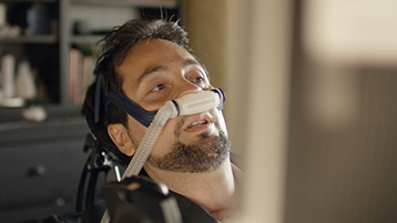 Victor Pineda uses a motorized wheelchai and ventilator while looking away.